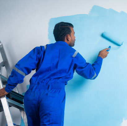 istockphoto-1457344132-612x612 Back view shot of painter doing painting work on wall with roller while standing on ladder - concept of - concept of hard working, blue collar job and home renovation