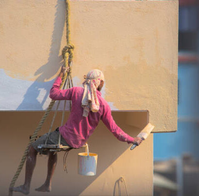 istockphoto-1469646695-612x612 WB. India-February 02, 2023. Unidentified Paint worker hanging on rope based tool to paint exterior of an old urban house.
